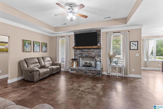 living room with ornamental molding, a tray ceiling, ceiling fan, and a stone fireplace