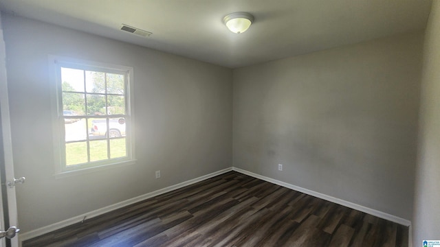 empty room featuring dark wood-type flooring, baseboards, and visible vents