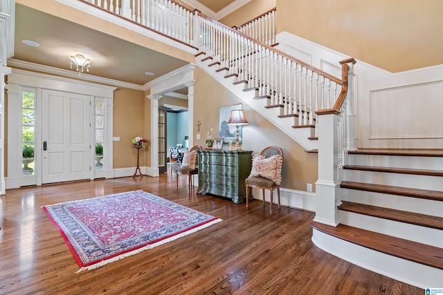 foyer entrance featuring ornate columns, a high ceiling, dark wood-type flooring, and crown molding