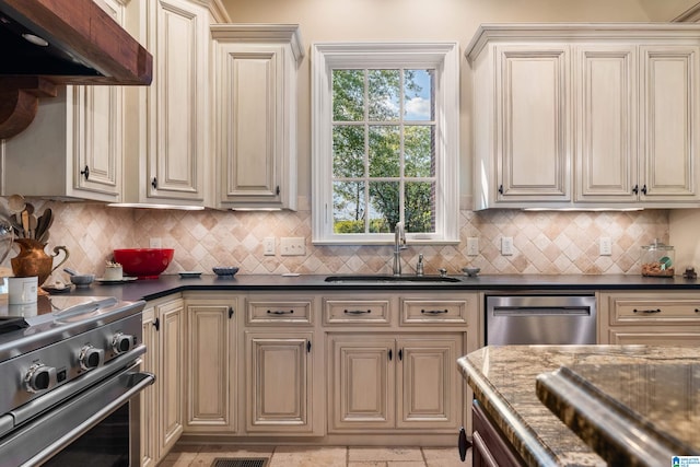 kitchen with decorative backsplash, dark stone countertops, cream cabinetry, and sink