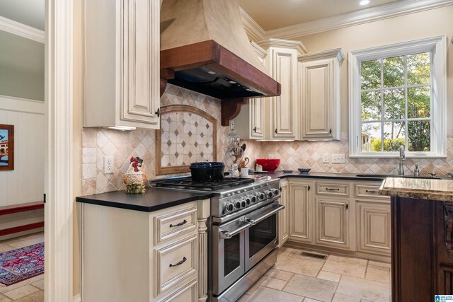 kitchen featuring custom exhaust hood, range with two ovens, cream cabinets, and sink