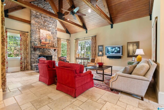 living room featuring beam ceiling, high vaulted ceiling, a stone fireplace, ceiling fan, and wooden ceiling