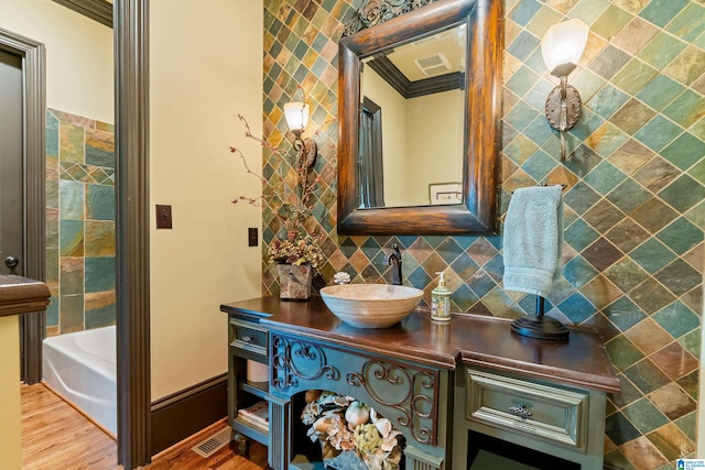 bathroom featuring tile walls, vanity, a bath, ornamental molding, and hardwood / wood-style floors