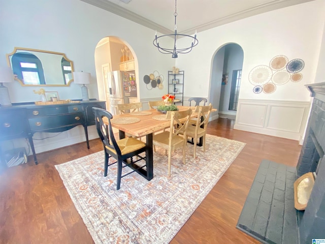 dining space featuring an inviting chandelier, dark hardwood / wood-style floors, a brick fireplace, and ornamental molding