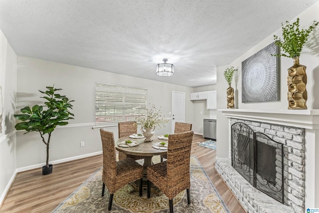 dining room featuring an inviting chandelier, a brick fireplace, a textured ceiling, and hardwood / wood-style flooring