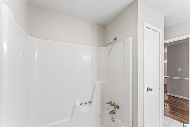 bathroom with hardwood / wood-style flooring and washtub / shower combination