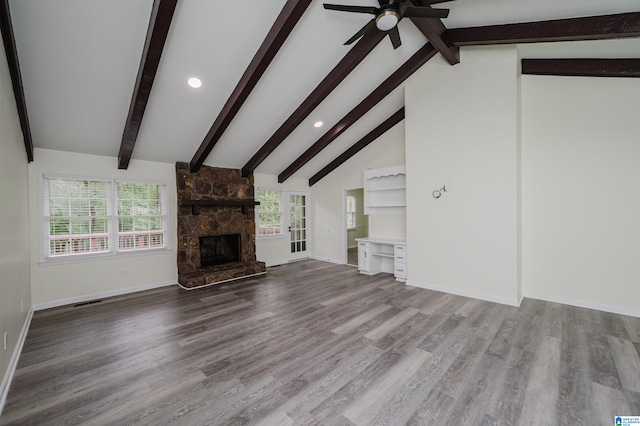 unfurnished living room featuring a stone fireplace, light hardwood / wood-style flooring, lofted ceiling with beams, and plenty of natural light