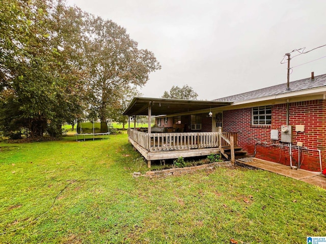 rear view of property featuring a lawn, a trampoline, and a deck