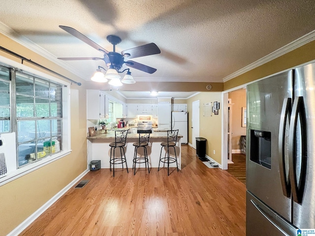 kitchen with white cabinets, ornamental molding, a textured ceiling, stainless steel appliances, and light wood-type flooring