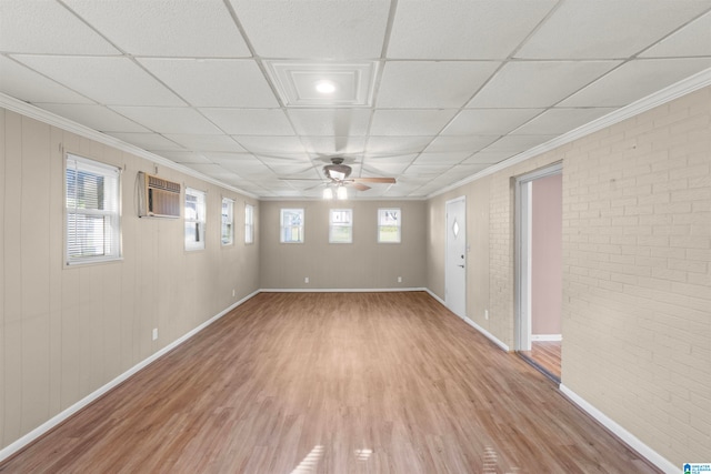 unfurnished room with brick wall, an AC wall unit, a drop ceiling, ceiling fan, and hardwood / wood-style flooring