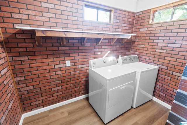 laundry room featuring brick wall, washing machine and dryer, light hardwood / wood-style flooring, and plenty of natural light