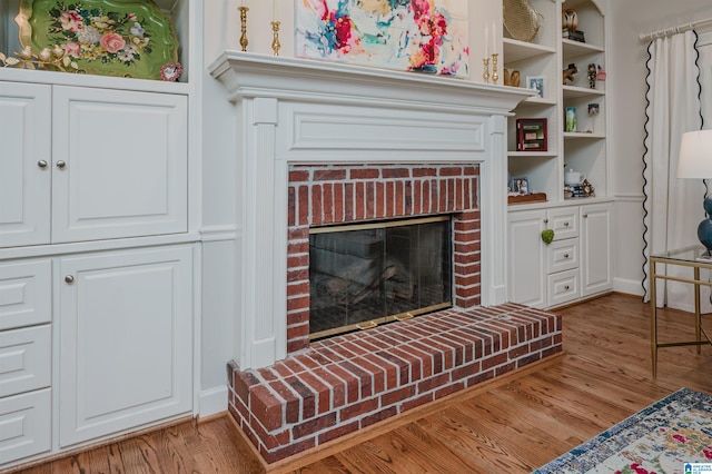 living room with a brick fireplace, light hardwood / wood-style floors, and built in features