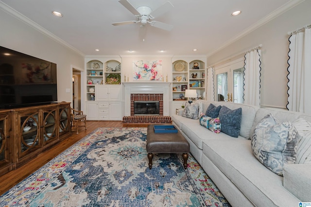 living room featuring ceiling fan, a fireplace, ornamental molding, and wood-type flooring