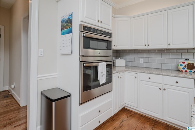 kitchen with white cabinets, backsplash, double oven, light stone countertops, and light hardwood / wood-style floors