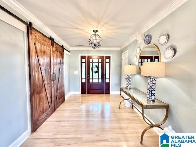 foyer entrance featuring hardwood / wood-style flooring, a barn door, ornamental molding, and a chandelier