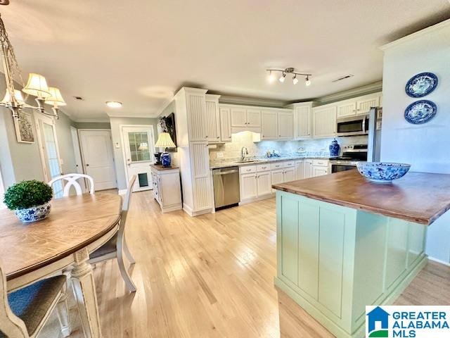 kitchen with appliances with stainless steel finishes, white cabinets, backsplash, light hardwood / wood-style flooring, and decorative light fixtures