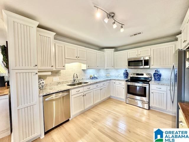 kitchen featuring appliances with stainless steel finishes, white cabinets, light stone countertops, light hardwood / wood-style flooring, and sink