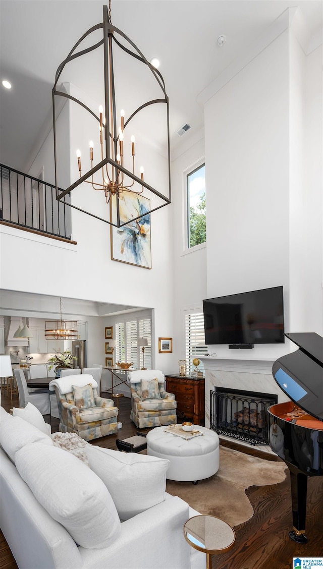 living room with a towering ceiling, a chandelier, hardwood / wood-style floors, and a fireplace