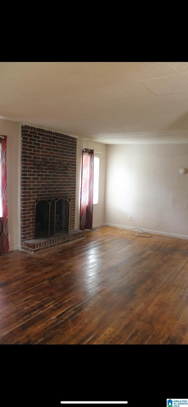 unfurnished living room with wood-type flooring, a brick fireplace, and a textured ceiling