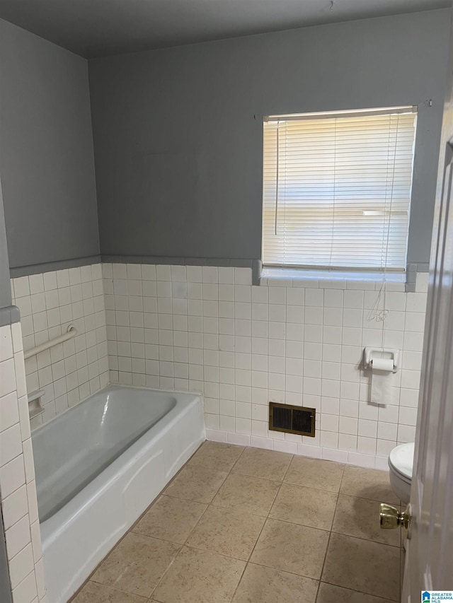 bathroom with tile walls, tile patterned floors, a bathtub, and toilet