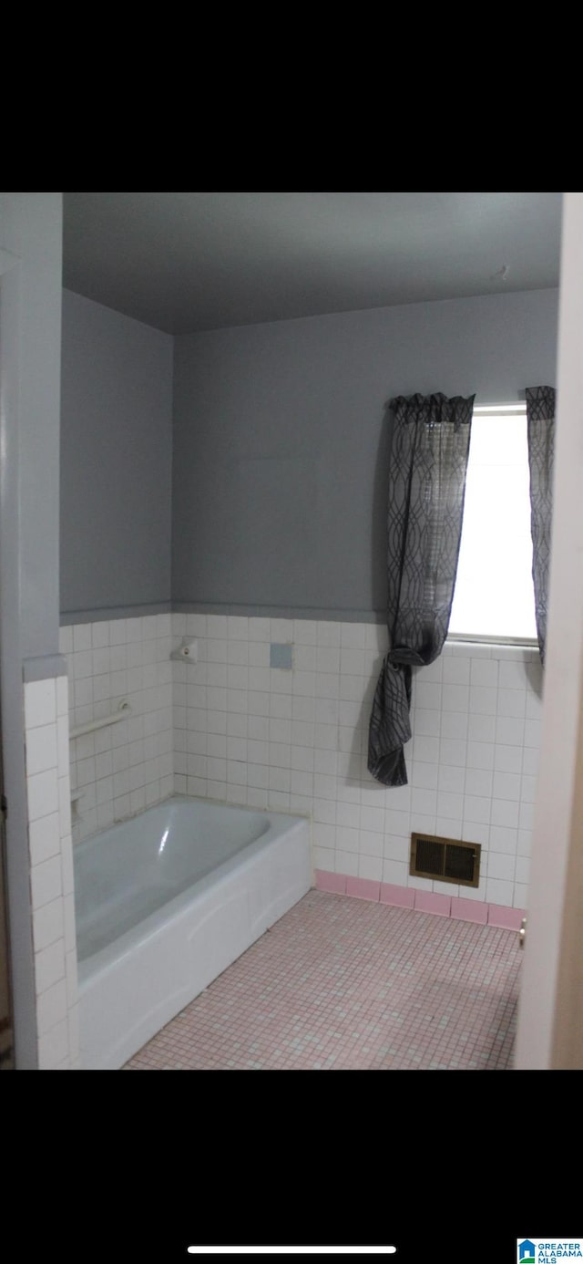 bathroom featuring tile patterned flooring, a bath, and tile walls