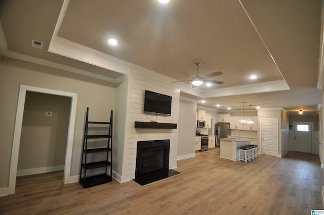 unfurnished living room featuring a tray ceiling, ceiling fan, light hardwood / wood-style floors, and a fireplace