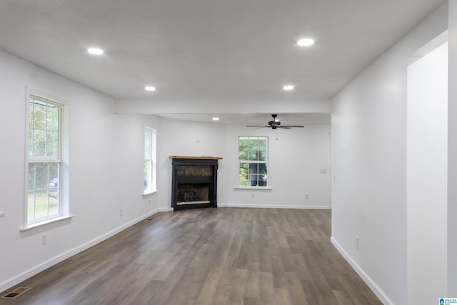 unfurnished living room with ceiling fan, dark wood-type flooring, and a wealth of natural light