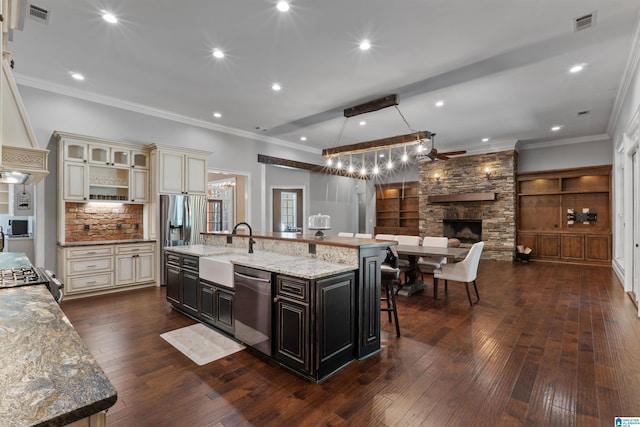 kitchen featuring sink, a large island with sink, cream cabinetry, appliances with stainless steel finishes, and a fireplace