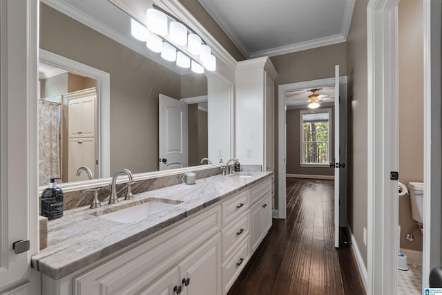 bathroom featuring ceiling fan, vanity, wood-type flooring, crown molding, and toilet