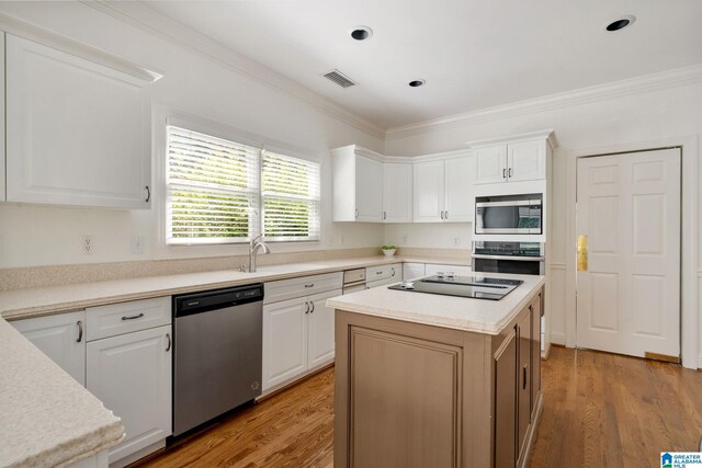 kitchen featuring white cabinetry, a kitchen island, stainless steel appliances, light wood-type flooring, and crown molding