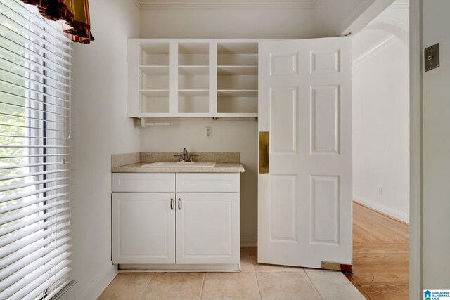 interior space with light tile patterned floors, sink, ornamental molding, and white cabinetry