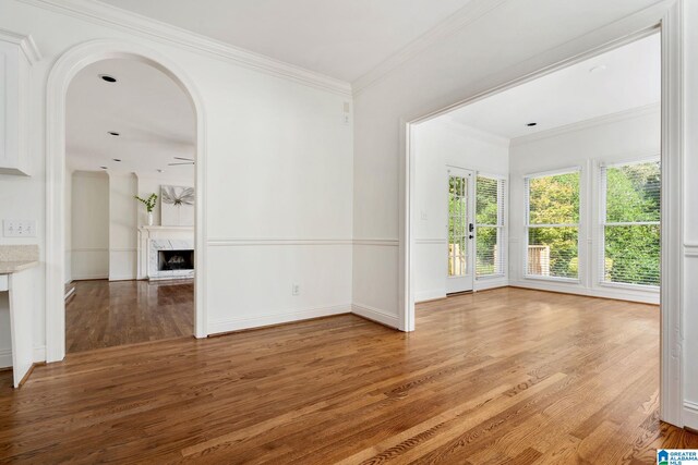 empty room featuring ceiling fan, hardwood / wood-style flooring, crown molding, and a high end fireplace