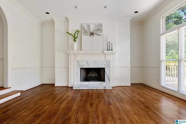 unfurnished living room featuring hardwood / wood-style flooring, ornamental molding, a high end fireplace, and a healthy amount of sunlight