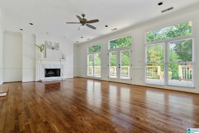 unfurnished living room with dark wood-type flooring, a fireplace, ceiling fan, french doors, and ornamental molding