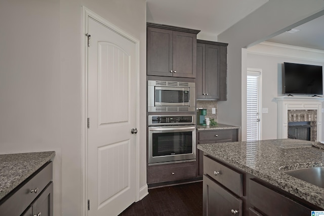 kitchen with light stone counters, ornamental molding, tasteful backsplash, appliances with stainless steel finishes, and dark hardwood / wood-style floors