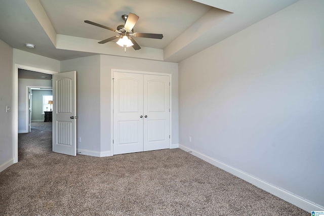 unfurnished bedroom featuring ceiling fan, a raised ceiling, and dark carpet