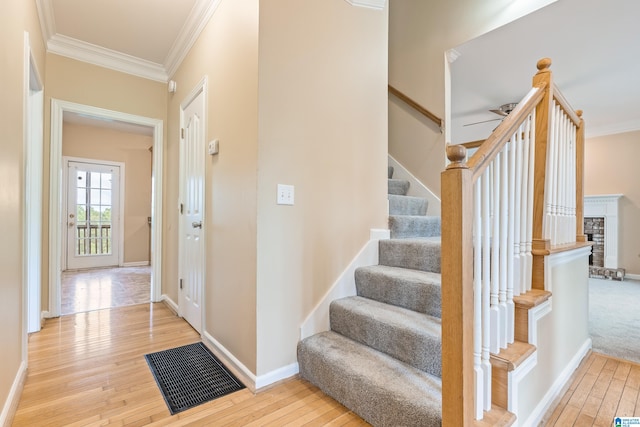 stairs featuring ornamental molding, ceiling fan, hardwood / wood-style flooring, and a fireplace