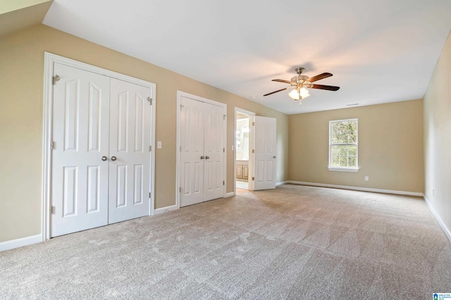 unfurnished bedroom featuring two closets, ceiling fan, and light colored carpet