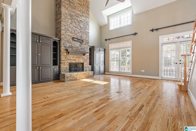 unfurnished living room featuring light hardwood / wood-style floors, high vaulted ceiling, a stone fireplace, ceiling fan, and decorative columns