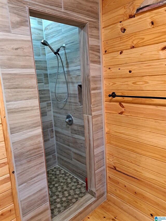 bathroom with tiled shower, wooden walls, and hardwood / wood-style floors