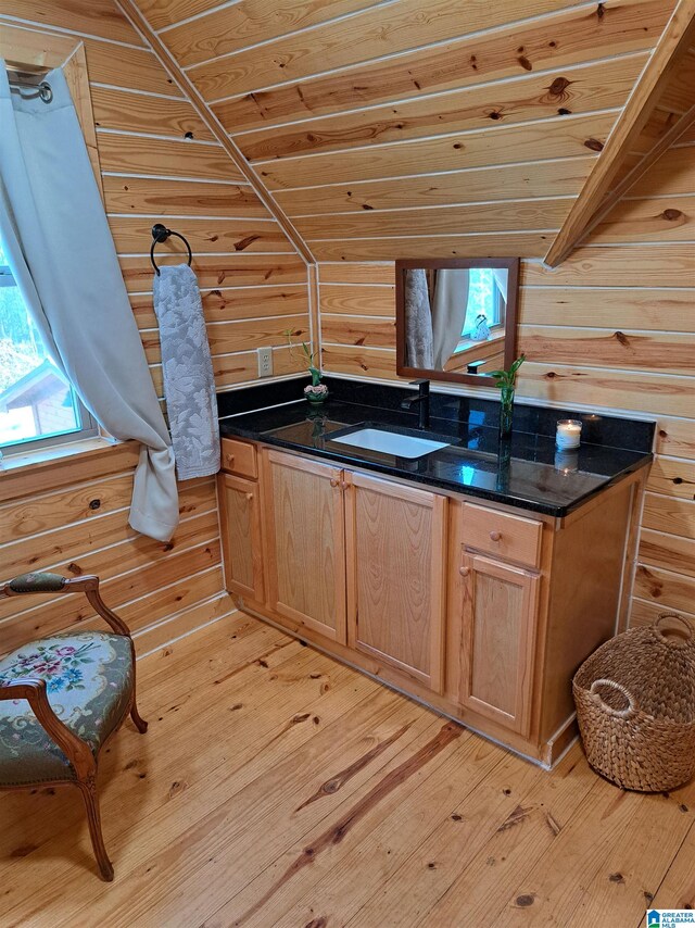 kitchen featuring wood walls, sink, wooden ceiling, dark stone countertops, and light hardwood / wood-style floors