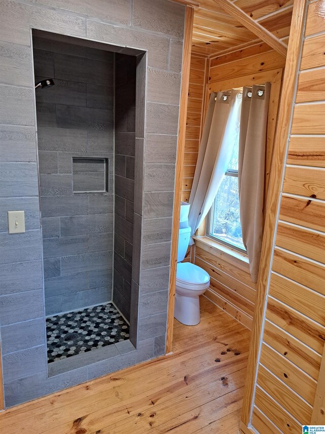 bathroom with wooden walls, tiled shower, wood-type flooring, and toilet