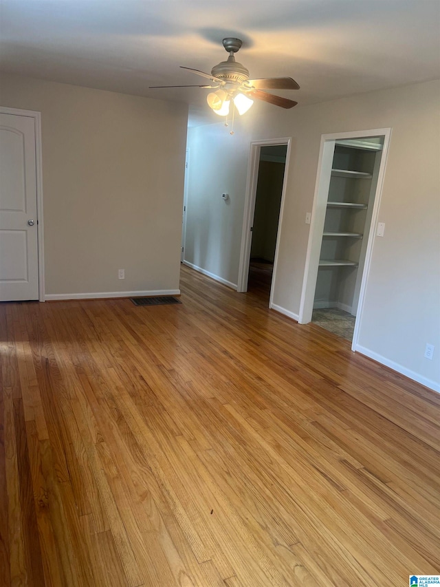 unfurnished room featuring built in shelves, light hardwood / wood-style floors, and ceiling fan