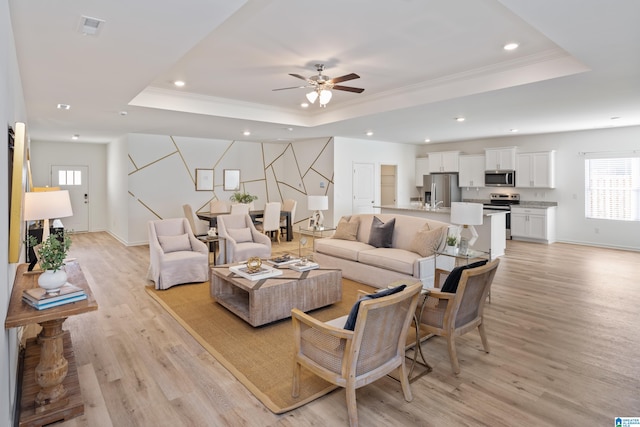 living room featuring ceiling fan, a tray ceiling, crown molding, and light hardwood / wood-style flooring