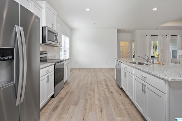 kitchen with appliances with stainless steel finishes, an island with sink, white cabinets, light hardwood / wood-style flooring, and sink