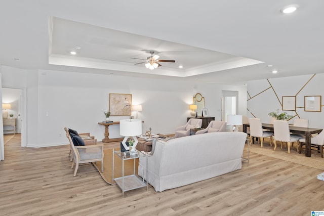 living room featuring crown molding, a tray ceiling, ceiling fan, and light hardwood / wood-style flooring