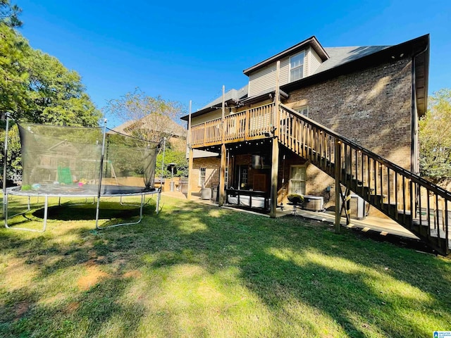 back of house with a wooden deck, a patio, a trampoline, and a lawn