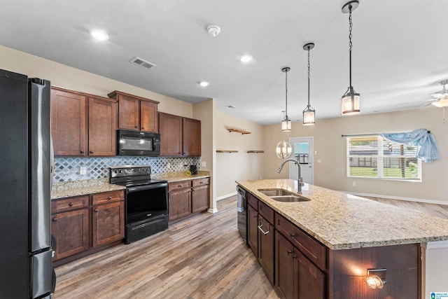 kitchen with an island with sink, light wood-type flooring, black appliances, and sink