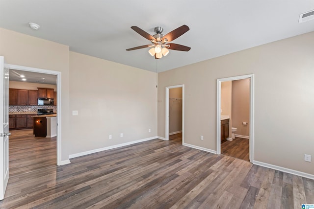 unfurnished bedroom with a closet, ensuite bath, a walk in closet, dark hardwood / wood-style flooring, and ceiling fan