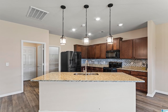 kitchen featuring light stone countertops, black appliances, a kitchen island with sink, dark hardwood / wood-style floors, and sink